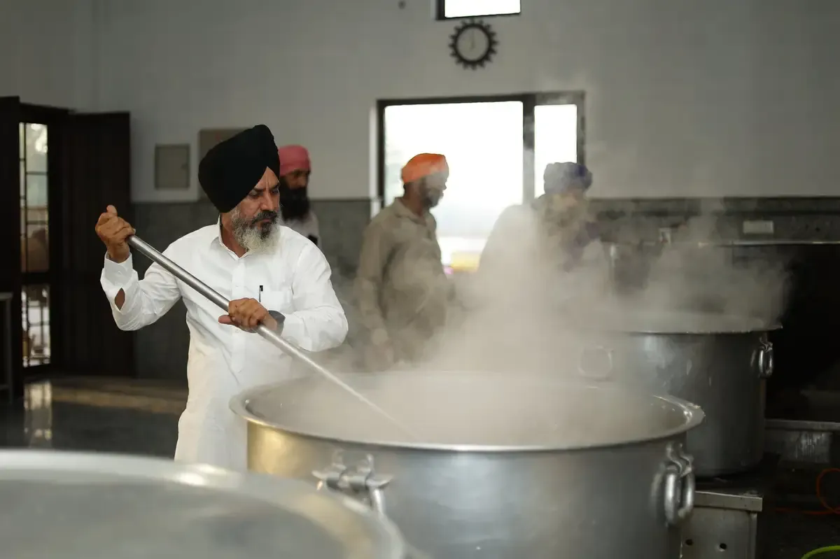 A sewadar stirring a large pot of Langar