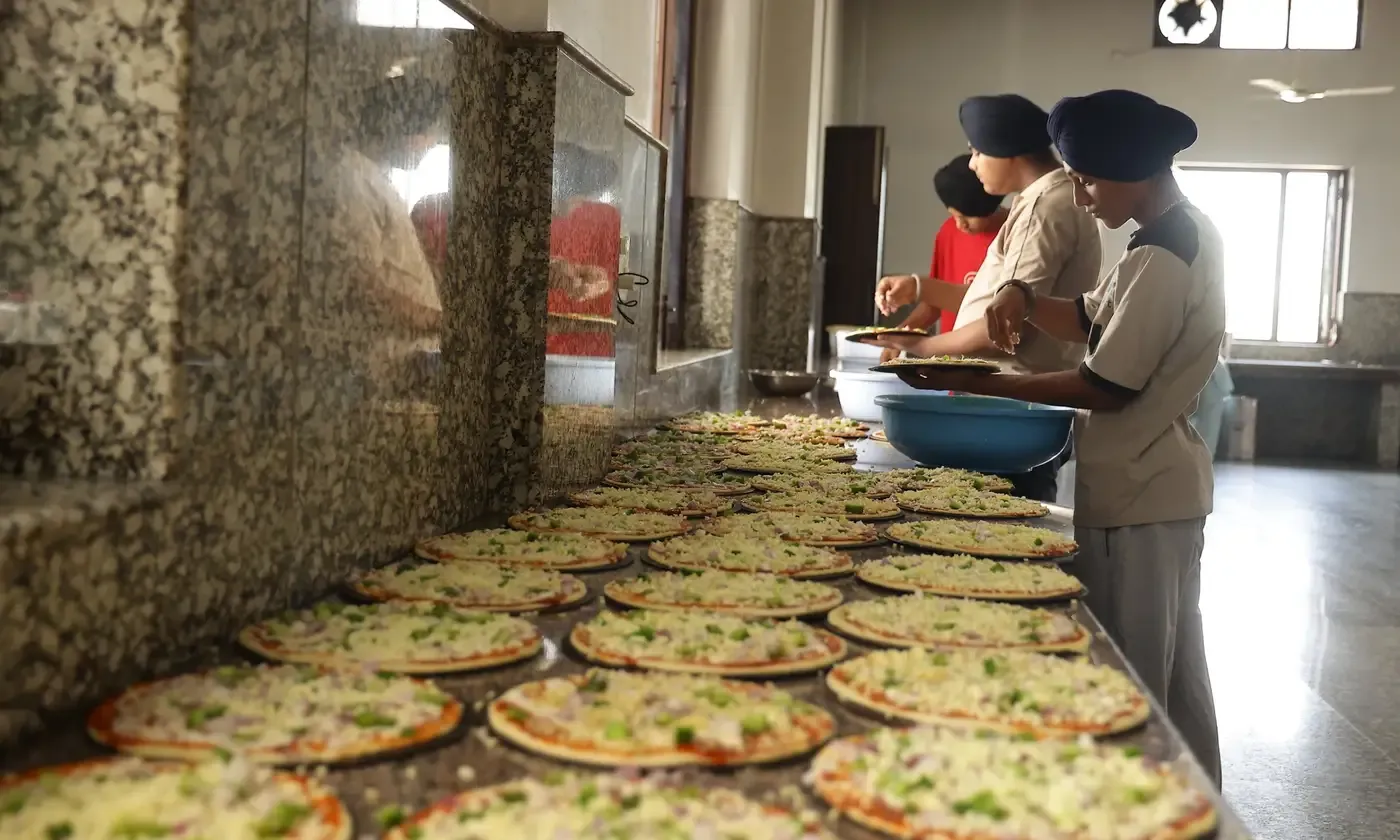Young sewadars topping pizzas for Sunday Pizza Langar